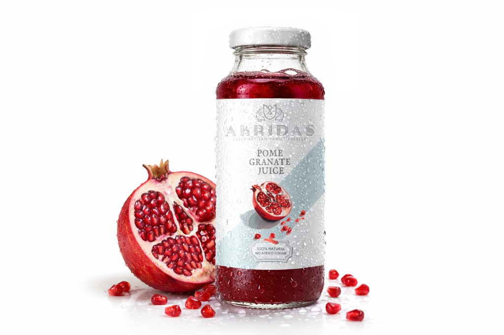 Akridas natural pomegranate juice in a glass bottle with fresh pomegranate half and arils on white